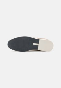 Zapato de ante marrón claro con suela de goma negra y entresuela crema. Presenta una textura suave y un diseño minimalista sin patrones ni acentos visibles.