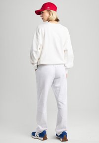 Felpa bianca con spalle scese, pantaloni di felpa grigi e un berretto rosso. Le sneaker presentano dettagli blu e una suola texture. Outfit casual.