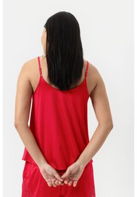 Canotta rossa con spalline sottili, texture morbida e vestibilità rilassata. Il retro presenta un design a scollatura bassa ed è abbinata a pantaloni corti coordinati.