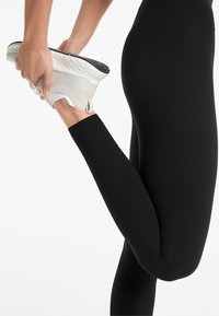 Leggings noirs en tissu lisse et extensible, associés à des baskets de couleur claire avec une semelle texturée et un matériau doux.