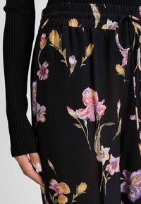 Tessuto floreale nero con cintura arricciata, caratterizzato da vivaci fiori rosa, viola e gialli. Dettagli delle maniche nere a coste visibili.