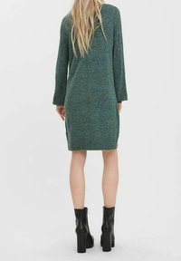 Robe verte en maille à manches longues, longueur mi-cuisse, fentes latérales, associée à des bottines à plateforme noires. Tissu texturé et coupe ajustée.