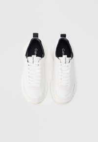 Adidașii albi cu partea superioară din suede neted și plasă, bot rotund și căptușeală interioară neagră în contrast. Prezintă șireturi și un etichetă cu logo pe toc.