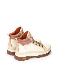 Botas de cuero blanco hasta el tobillo con suela marrón, que cuentan con un collar acolchado, herrajes dorados y acentos texturizados. Logo de Vibram visible en la suela.