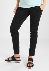 Pantalons en coton extensible noirs avec une coupe slim et des poches latérales, associés à des sandales noires avec de larges lanières et des semelles blanches.