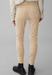 Pantaloni in velluto a coste beige con una vestibilità slim, caratterizzati da tasche posteriori e una texture sottile, abbinati a stivaletti neri alla caviglia.