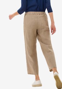 Pantalon en lin beige à coupe décontractée, doté d'une taille élastique, de poches latérales et d'un détail bouton à l'arrière. Texture lisse et longueur raccourcie.