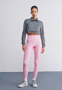 Grå kort sweatshirts med bølgekant, kombinert med tettsittende lyserosa leggings. Har hvite side-striper og grå sneakers.
