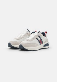 Zapatillas deportivas de color gris claro con parte superior de malla y acentos de gamuza. Presenta rayas en azul marino y rojo, cordones blancos y suela de goma.