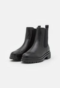 Botas Chelsea de cuero negro con paneles laterales elásticos, tirador y suela resistente. Textura suave con punta redondeada y tacón grueso.