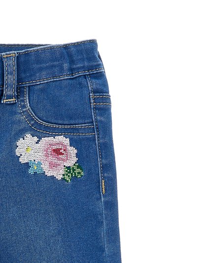 Μπλε τζιν τζιν με μικρό κεντητό λουλουδένιο σχέδιο κοντά στην μπροστινή τσέπη, με ροζ, λευκά, μπλε λουλούδια και πράσινα φύλλα.