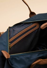 Interieur van een marineblauwe stoffen tas met een ritssluitingvak met blauwe polkadots, bruine ritsaccenten en gouden rits tanden.