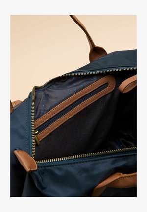 Innenansicht einer dunkelblauen Stofftasche mit einem Reißverschlusstasche, blauem Tupfenmuster, braunen Reißverschlussakzenten und goldfarbenen Reißverschlusszähnen.