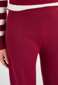 Pantalons tricotés rouges avec une texture douce et un design de ceinture. La vue en gros plan montre une finition lisse et des détails de couture subtils.