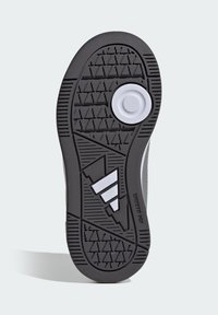 Suela de zapato de goma negra con patrón texturizado antideslizante, con un acento circular blanco y tres rayas blancas en el lateral.