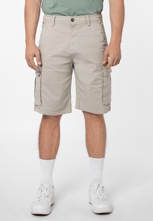 Man wearing beige cargo shorts, white socks, white sneakers, and a green t-shirt, standing against a plain white background.