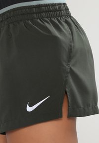 Tummanvihreät Nike-shortsit, joissa on joustava vyötärö, sivuhalkiot ja valkoinen logo vasemmassa alareunassa. Silkyntuntuinen, kevyt kangas.