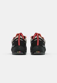 Schwarz und graue Sportschuhe mit einer strukturierten Oberfläche und roten Akzenten. Dicke Sohlen und kontrastierende farbige Hardware bieten Stabilität.