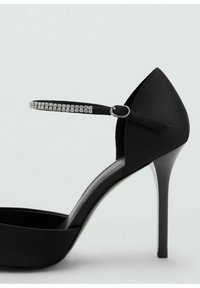 Scarpa nera con tacco alto, finitura in satin, punta affusolata e sottile tacco a stiletto. Presenta una cinghia alla caviglia decorata con strass.