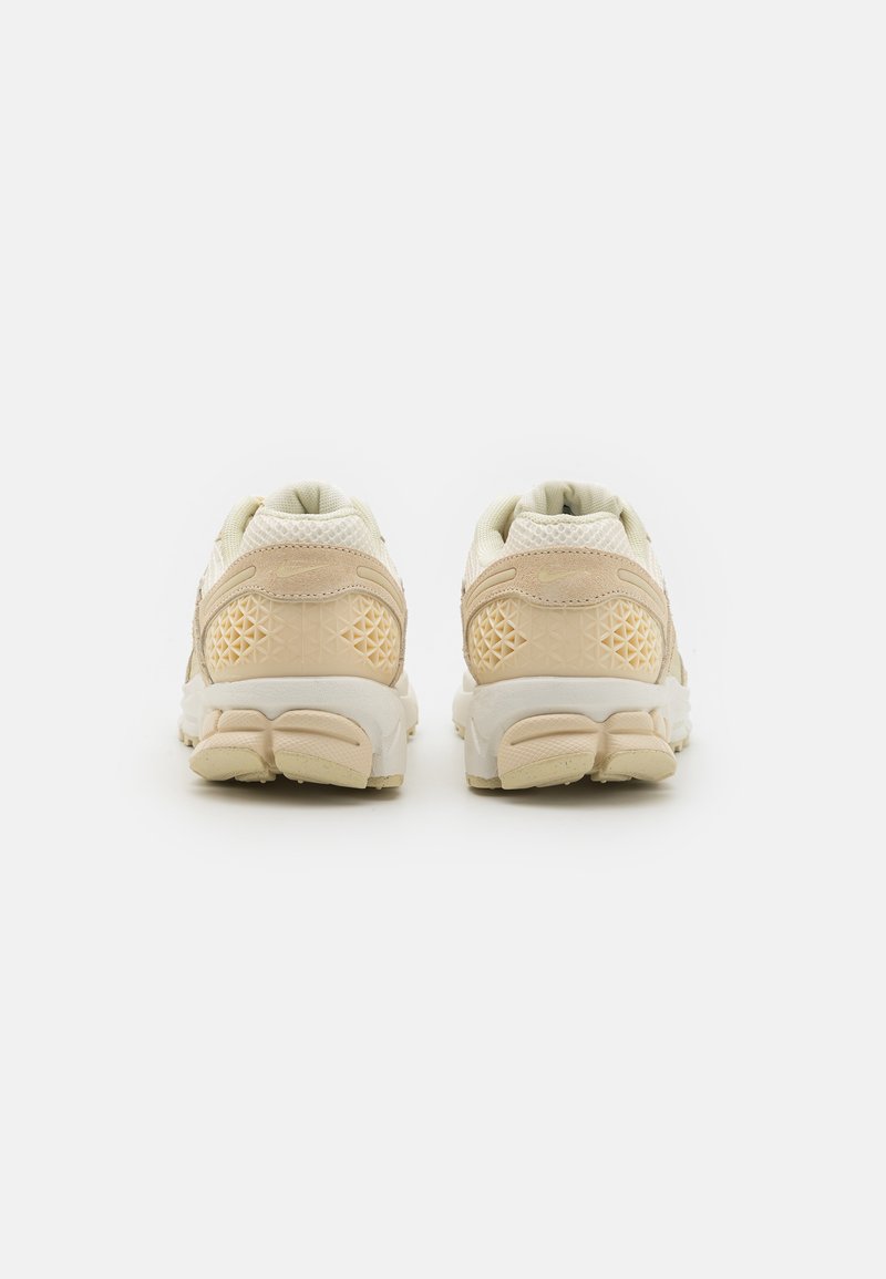 Zapatillas deportivas blancas y beige con parte superior de malla texturizada, cuello acolchado y una suela de goma gruesa con detalles de patrón geométrico.