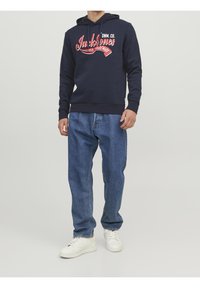 Námořnická mikina s bílým a červeným grafickým potiskem, spárovaná s volnými modrými džíny a bílými teniskami. Jednoduchý design, pohodlný střih.