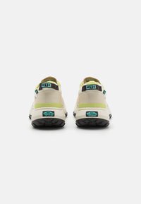 Două adidași bej cu accente în galben pal, maro deschis și teal. Prezintă o talpă neagră robustă și un material superior texturat. Branding MTE.