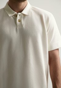 Piké skjorte i teksturert off-white stoff, med klassisk krage, to knappeåpning og kortermet.