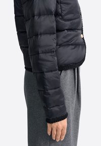 Giubbotto puffer trapuntato nero con taglio cropped, caratterizzato da un bordo testurizzato nero all'orlo e ai polsini. Tessuto liscio e lucido con una tasca con zip.
