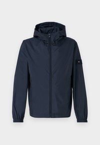 Marineblauwe waterdichte jas met capuchon, elastische manchetten, een rits aan de voorkant en een borstzak met een logo. Glad textuur en lichtgewicht ontwerp.