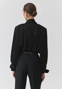 Black, flowy blouse with puffed sleeves and a gathered neckline, paired with tailored black trousers featuring side pockets and a belt.