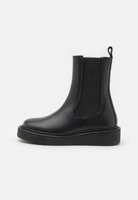 Černá kožená kotníková bota s elastickými bočními panely a texturovanou podrážkou. Má poutko na zadní straně a prošívání podél podrážky.