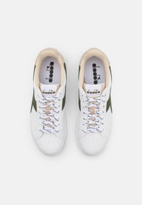 Sneaker bianche con dettagli in suede verde, linguetta beige e lacci bianchi. Presentano una punta perforata e una soletta con marchio per un ulteriore tocco di dettaglio.