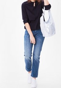 Marinblus med nyckelhålsringning, uppvikta ärmar; ljusblå slitna jeans; silverfärgad metallhandväska; vita sneakers.