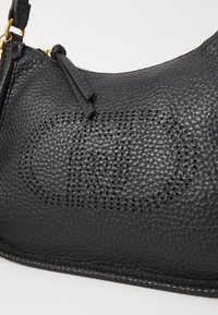 Black textured leather handbag with perforated circular logo design and gold-tone hardware on a white background.