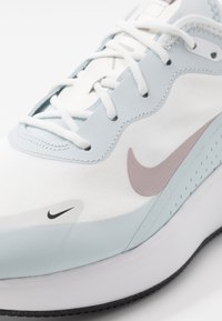 Vaaleansininen ja valkoinen urheilukenkä, jossa on sileä päällinen, verkkomaisia yksityiskohtia, erottuvat vaaleanpunaiset yksityiskohdat ja musta kumipohja.