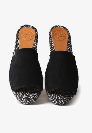 Chaussures noires en daim à enfiler avec un bout ouvert, une semelle espadrille tissée noire et blanche, et une semelle intérieure en cuir fauve avec des lettres embossées.