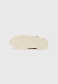 Valge sneaker'i tald, millel on reljeefne kiri "EXCHANGE." Tekstureeritud viimistlus ja kerge kõverus varvaste suunas; minimalistlik disain, ilma nähtavate mustriteta.