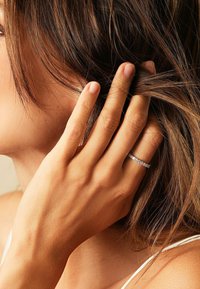 Anello d'argento con molte piccole pietre, indossato su una mano che tocca i capelli, mostrando una texture della pelle liscia e capelli castani chiari.