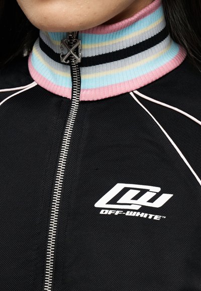 Κοντινό πλάνο μαύρου ενδύματος με φερμουάρ, με πολύχρωμο ριγέ γιακά και το λογότυπο "Off-White" στο στήθος.