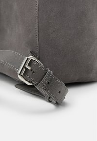 Szara zamszowa torba z teksturowanym wykończeniem, gładkim szarym skórzanym uchwytem oraz metalowym zapięciem z detalami w stylu przeszycia na pasku.