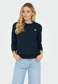 Sweatshirt bleu marine en matériau doux, avec un petit logo d'ours doré sur la poitrine. Poignets et taille ajustés avec un design classique.