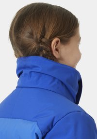 Modrá bunda s vysokým límcem, hladkým materiálem a elegantním designem. Viditelné švy zdůrazňují strukturu.