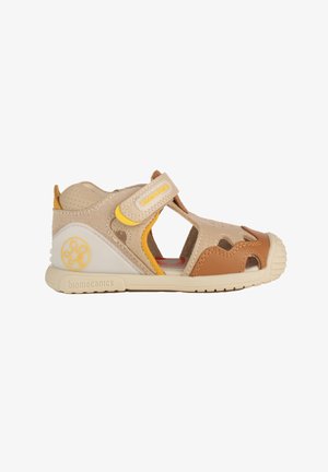 Sandalo per bambini beige e marrone con punta aperta, cinturino in velcro, pelle traforata e suola in gomma progettato per comfort e supporto.