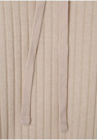 Beżowa tkanina o fakturze z pionowymi prążkami; na krawędzi umieszczono dwa płaskie, plecione sznurki, co dodaje funkcjonalności do projektu.
