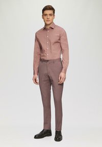 Helles rosa Langarmhemd kombiniert mit figurbetonten, dunkelrosanen Hosen. Das Outfit umfasst schwarze Schuhe und ein maßgeschneidertes Design.