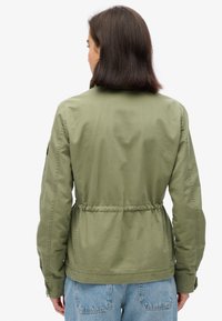 Olijfgroene, lichtgewicht jas met een trekkoord in de taille, lange mouwen en een gladde textuur. Bevat subtiele stiksels en geen zichtbare hardware.