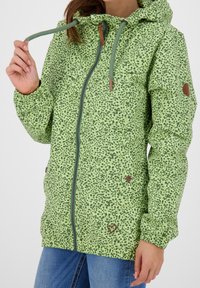 Zielona kurtka w kwiatowy wzór z zamkiem z przodu, kapturem ze sznurkiem i elastycznymi mankietami. Posiada brązowe akcenty i dwie przednie kieszenie.