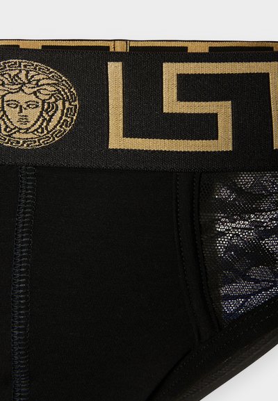 Μαύρο εσώρουχο με χρυσό ζωνάκι με σχέδιο ελληνικού κλειδιού και λογότυπο Μέδουσας, με δίχτυ στα πλαϊνά πάνελ που έχουν περίτεχνα μοτίβα.