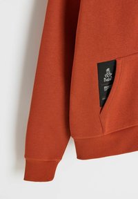 Pomarańczowa bluza z prążkowanymi mankietami i pasem dolnym. Posiada boczną kieszeń i etykietę z logo na kieszeni, wykonana z miękkiej bawełnianej tkaniny.