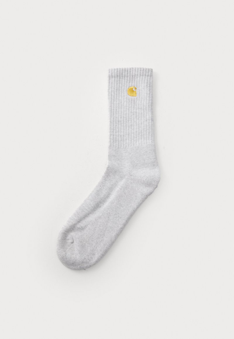Calcetín gris acanalado hecho de un material suave, con un logo amarillo en el puño. El diseño es simple y la forma es estándar para calcetines.